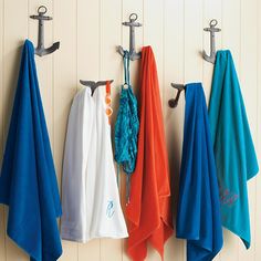 three towels hanging from hooks on a wall next to two towel racks and an umbrella