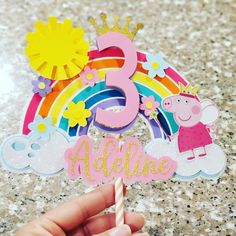 a hand holding up a birthday card with the number five on it and a rainbow in the background