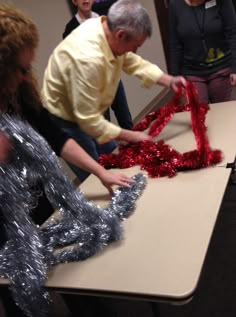 two people sitting at a table making red and silver decorations with tinsel on them