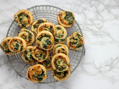 small appetizers with spinach and cheese are on a wire rack atop a marble countertop