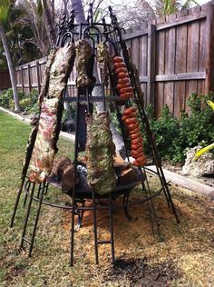 an outdoor grill with hot dogs on it in the grass next to a wooden fence