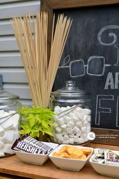 a table topped with lots of food next to a chalkboard and some jars filled with marshmallows