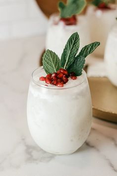 a dessert in a glass with berries and leaves on top, sitting on a table