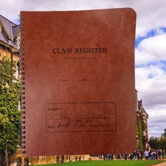 a large brown book sitting on top of a lush green field next to a tall building