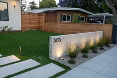 a modern home with grass and landscaping in the front yard at dusk, including steps leading up to an address sign