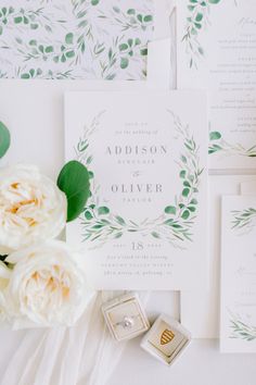 the wedding stationery is laid out on top of each other, with white flowers and greenery