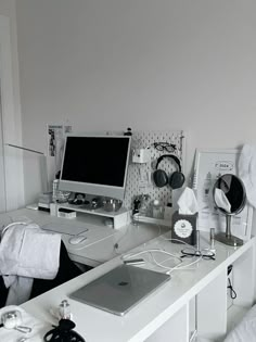 a white desk topped with a computer monitor next to a keyboard and headphones on top of it