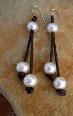 three white pearls are hanging from brown leather earwires on a piece of stone