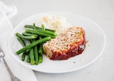 a white plate topped with meat, green beans and mashed potatoes next to a fork