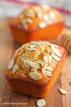 two muffins with almonds sitting on top of a wooden cutting board