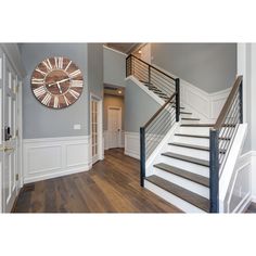 a clock mounted to the side of a wall next to a stair case in a home