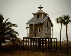 an old wooden house sitting on top of a pier next to palm trees and water