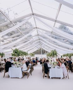 a group of people sitting at tables under a white tented area filled with plants