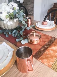 the table is set with white and gold plates, silverware, and pumpkins