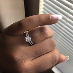 a woman's hand with a diamond ring on her finger, next to a window