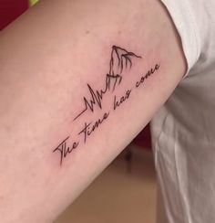 a tattoo saying the time has come on someone's left arm with mountains in the background