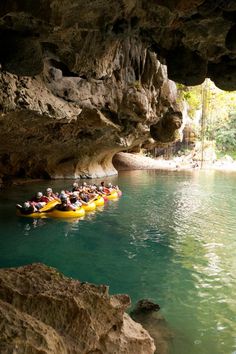 a group of people riding on top of yellow rafts down a river under a cave