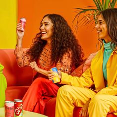 two women sitting on a couch and one is holding a can of coca - cola