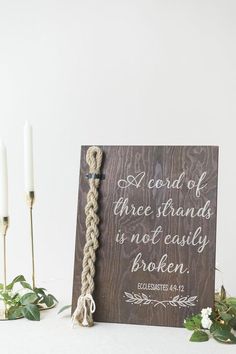 a wooden sign with a rope attached to it next to some candles and greenery