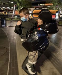 a boy wearing a face mask and carrying a backpack while walking down a sidewalk at night