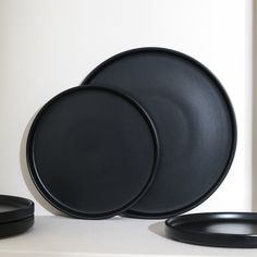 three black plates sitting next to each other on a white counter top with one empty plate in the middle