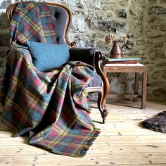 a chair with a plaid blanket on it in front of a stone wall and wooden floor