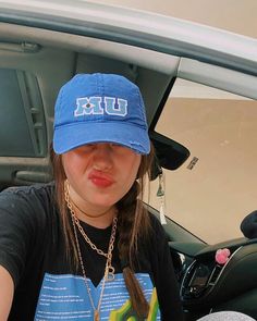 a young woman wearing a blue hat sitting in the back seat of a car with her tongue out