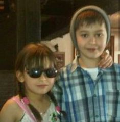 two young children standing next to each other with sunglasses on their heads and one holding up his arm