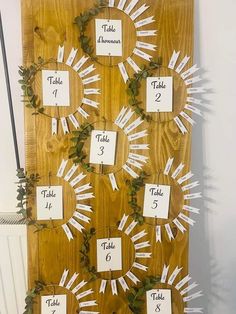 the table numbers are arranged on a wooden board with greenery and white tags attached to it