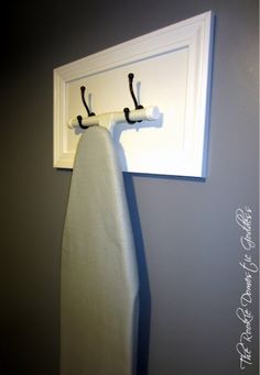 an ironing board is hanging on the wall next to a towel rack with two hooks