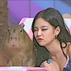 a woman sitting next to a rodent on top of a pink and white chair