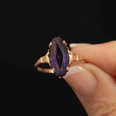 This very pretty handmade 10k gold ring features a striking marquise-shaped purple synthetic glass stone, crafted to resemble an amethyst. The gem, measuring 20mm x 7mm, shows some wear on the surface but remains free of chips, adding character to this unique piece. The design of the ring suggests it may have originally held an Alaskan black diamond, making this replacement with the purple stone a distinctive and creative choice. Crafted with care and attention to detail, this ring is a size 8.2 Marquise Amethyst Ring Gemstone Gift, Marquise Amethyst Ring Gift, Marquise Amethyst Ring As Gift, Gift Marquise Amethyst Ring, Marquise Amethyst Jewelry Gift, Marquise Amethyst Jewelry For Gift, Gold Marquise Amethyst Ring, Gift Marquise Amethyst Jewelry, Fine Jewelry 14k Gold Marquise Amethyst Ring