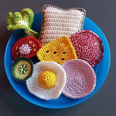 crocheted items are arranged on a blue plate with a flower and an egg