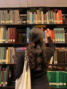 a woman standing in front of a bookshelf holding a bag and looking up