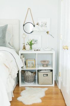 a bedroom with white walls and wooden flooring is pictured in this image, there are baskets on the shelf next to the bed