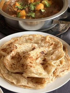 some food is on a white plate near a pot of soup and a silver bowl