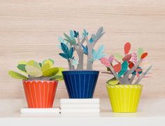 three colorful flower pots sitting on top of a white shelf next to books and planters