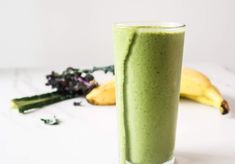 a green smoothie in a tall glass next to two bananas