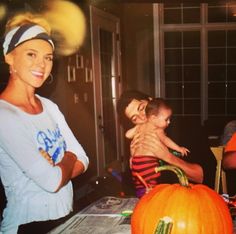 a woman holding a child next to a pumpkin