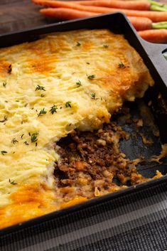 a casserole dish with meat, cheese and carrots on the table next to it