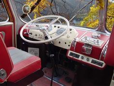 the interior of an old car with red leather seats and steering wheel in front of trees