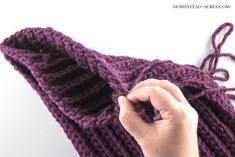 a hand is holding the end of a purple knitted hat