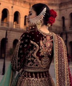 a woman in a red and gold bridal outfit with flowers on her head, looking off to the side