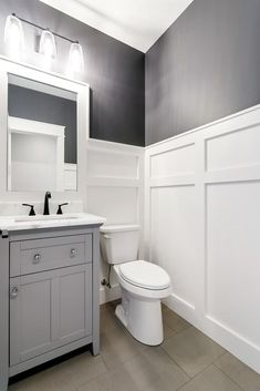 a white toilet sitting next to a sink in a bathroom under a mirror and two lights