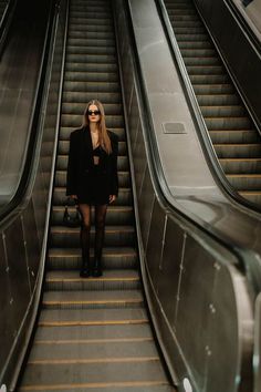 a woman is standing on an escalator with her hand in her pocket and looking at the camera