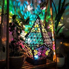 a colorful lamp sitting on top of a wooden shelf next to plants and potted plants