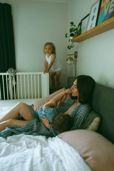 a woman laying on top of a bed next to a baby in a crib