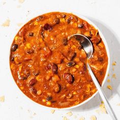 a white bowl filled with chili and beans on top of a table next to a spoon