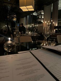 a restaurant with menus and wine glasses on the table in front of it at night