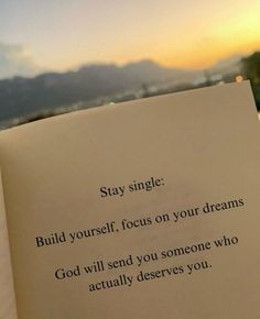 an open book sitting on top of a bed next to a window with the words stay single build yourself, focus on your dreams